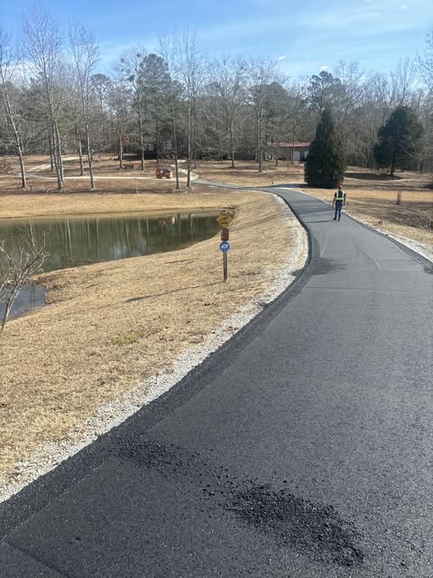 Finished curved asphalt driveway beside a pond